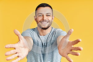 Handsome happy man with open hand ready for hugs on yellow background