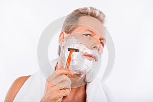 Handsome happy man with towel shaving himself with a razor