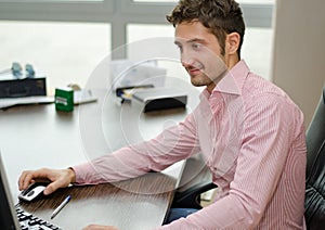 Handsome, happy office worker smiling while using computer