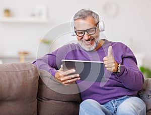 Handsome happy senior man waving by hand while talking online on digital tablet with family