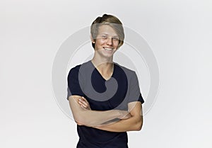 Handsome happy smiling young man wearing black t-shirt with crossed arms studio portrait against white wall