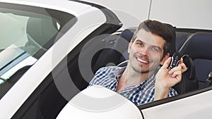 Handsome happy young male driver holding car keys sitting in his auto