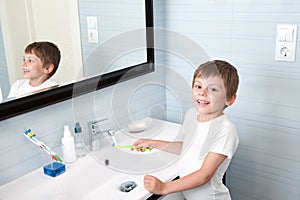 Handsome healthy boy washing toothbrush over washbasin photo