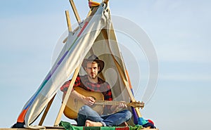 Handsome hiker man with guitar in tent. Male cowboy in camping.