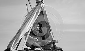 Handsome hiker man with guitar in tent. Male cowboy in camping.