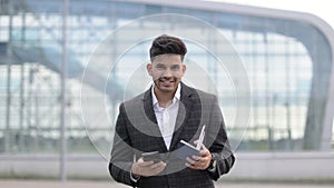 Handsome hindu man holding cell phone, passport and boarding pass checking his flight schedule.