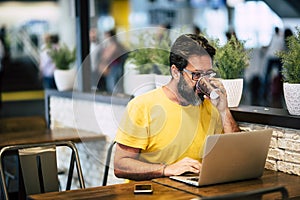 Handsome hipster bearded man drink coffee at the coworking space and work with laptop computer and internet free wifi connection