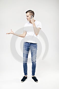 Handsome hipster guy full-length standing talking by phone and swears, isolated on white background