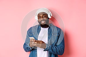 Handsome hipster guy in headphones smiling satisfied at camera, listening music in headphones, using mobile app