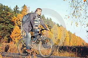 Handsome hipster man in casual wear with backpack riding bicycle in autumn park or forest. Discovery beautiful fall season