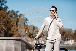 Handsome hipster at park. Businessman with bicycle speaks on phone