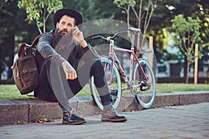 A handsome hipster traveler with a stylish beard and tattoo on his arms dressed in casual clothes and hat with a bag