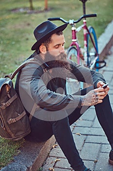 A handsome hipster traveler with a stylish beard and tattoo on his arms dressed in casual clothes and hat with a bag