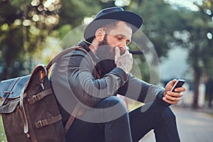 A handsome hipster traveler with a stylish beard and tattoo on his arms dressed in casual clothes and hat with a bag