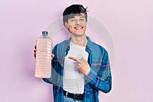 Handsome hipster young man holding detergent bottle smiling happy pointing with hand and finger