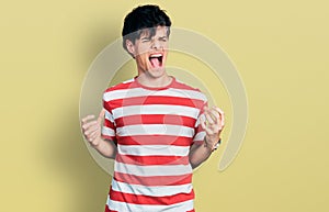 Handsome hipster young man wearing casual striped t shirt crazy and mad shouting and yelling with aggressive expression and arms