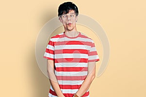 Handsome hipster young man wearing casual striped t shirt making fish face with lips, crazy and comical gesture