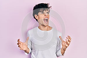 Handsome hipster young man wearing casual white shirt crazy and mad shouting and yelling with aggressive expression and arms