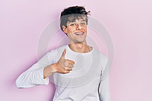 Handsome hipster young man wearing casual white shirt doing happy thumbs up gesture with hand