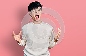 Handsome hipster young man wearing casual winter sweater crazy and mad shouting and yelling with aggressive expression and arms