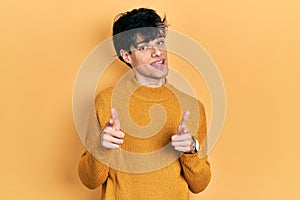 Handsome hipster young man wearing casual yellow sweater pointing fingers to camera with happy and funny face