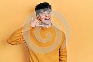 Handsome hipster young man wearing casual yellow sweater smiling doing phone gesture with hand and fingers like talking on the