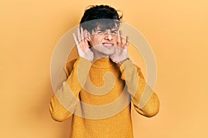 Handsome hipster young man wearing casual yellow sweater trying to hear both hands on ear gesture, curious for gossip