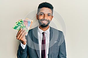 Handsome hispanic business man with beard holding south african rand banknotes looking positive and happy standing and smiling