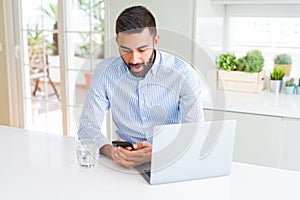 Handsome hispanic business man using laptop and smartphone scared in shock with a surprise face, afraid and excited with fear