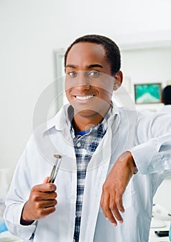 Handsome hispanic dentist wearing white doctors coat and holding dental tool while smiling posing to camera