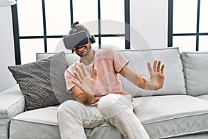 Handsome hispanic man afraid wearing virtual reality glasses at the living room at home