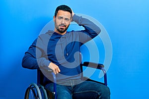 Handsome hispanic man with beard sitting on wheelchair confuse and wonder about question