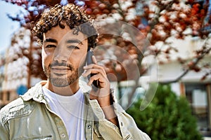 Handsome hispanic man with beard smiling happy outdoors on a sunny day having a conversation speaking on the phone