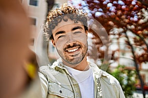 Handsome hispanic man with beard smiling happy outdoors on a sunny day taking a selfie photo