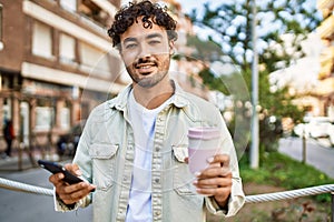 Handsome hispanic man with beard smiling happy outdoors on a sunny day using smartphone