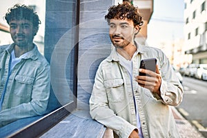 Handsome hispanic man with beard smiling happy outdoors on a sunny day using smartphone