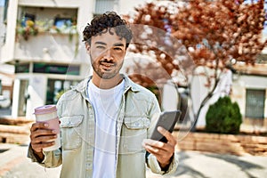 Handsome hispanic man with beard smiling happy outdoors on a sunny day using smartphone