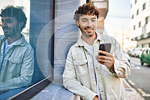 Handsome hispanic man with beard smiling happy outdoors on a sunny day using smartphone