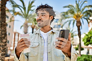 Handsome hispanic man with beard smiling happy outdoors on a sunny day using smartphone