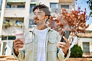 Handsome hispanic man with beard smiling happy outdoors on a sunny day using smartphone