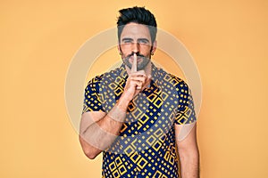 Handsome hispanic man with beard wearing 80s disco style shirt asking to be quiet with finger on lips