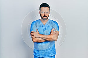 Handsome hispanic man with beard wearing blue male nurse uniform skeptic and nervous, disapproving expression on face with crossed