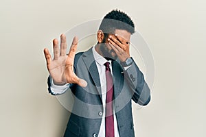 Handsome hispanic man with beard wearing business suit and tie covering eyes with hands and doing stop gesture with sad and fear