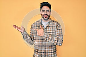 Handsome hispanic man with beard wearing casual clothes amazed and smiling to the camera while presenting with hand and pointing