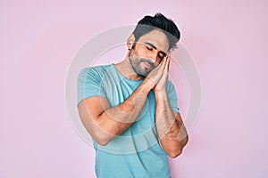 Handsome hispanic man with beard wearing casual clothes sleeping tired dreaming and posing with hands together while smiling with