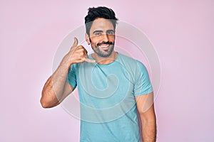 Handsome hispanic man with beard wearing casual clothes smiling doing phone gesture with hand and fingers like talking on the