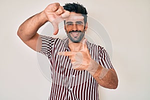 Handsome hispanic man with beard wearing casual clothes smiling making frame with hands and fingers with happy face
