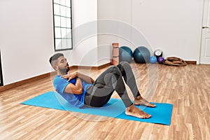 Handsome hispanic man doing exercise and stretching on yoga mat, practicing flexibility and training at the gym