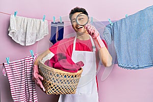 Handsome hispanic man doing laundry holding wicker basket looking for a stain smiling and laughing hard out loud because funny