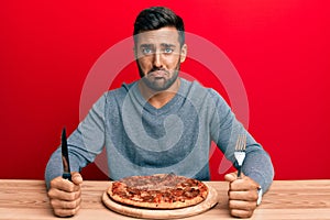 Handsome hispanic man eating tasty pepperoni pizza depressed and worry for distress, crying angry and afraid
